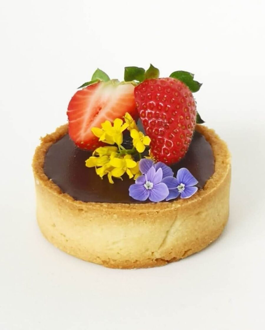 Homemade mini chocolate tartlets with almond crust, decorated with strawberries and edible flowers